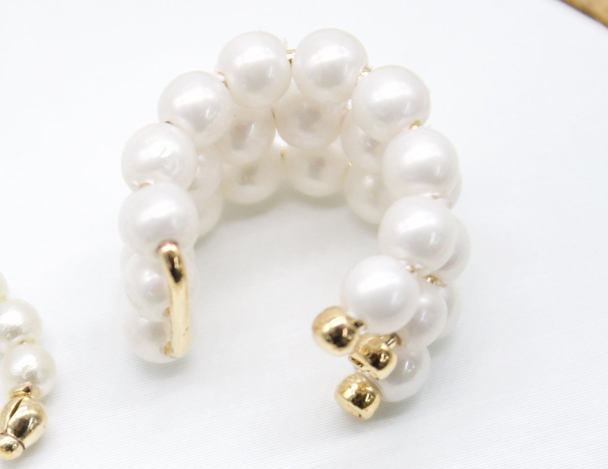 A multi-row faux pearl ear cuff features glossy white beads and polished gold accents against a clean white background.