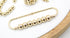 A gold safety pin brooch embellished with a row of shiny metallic beads rests on a white surface next to matching jewelry pieces.