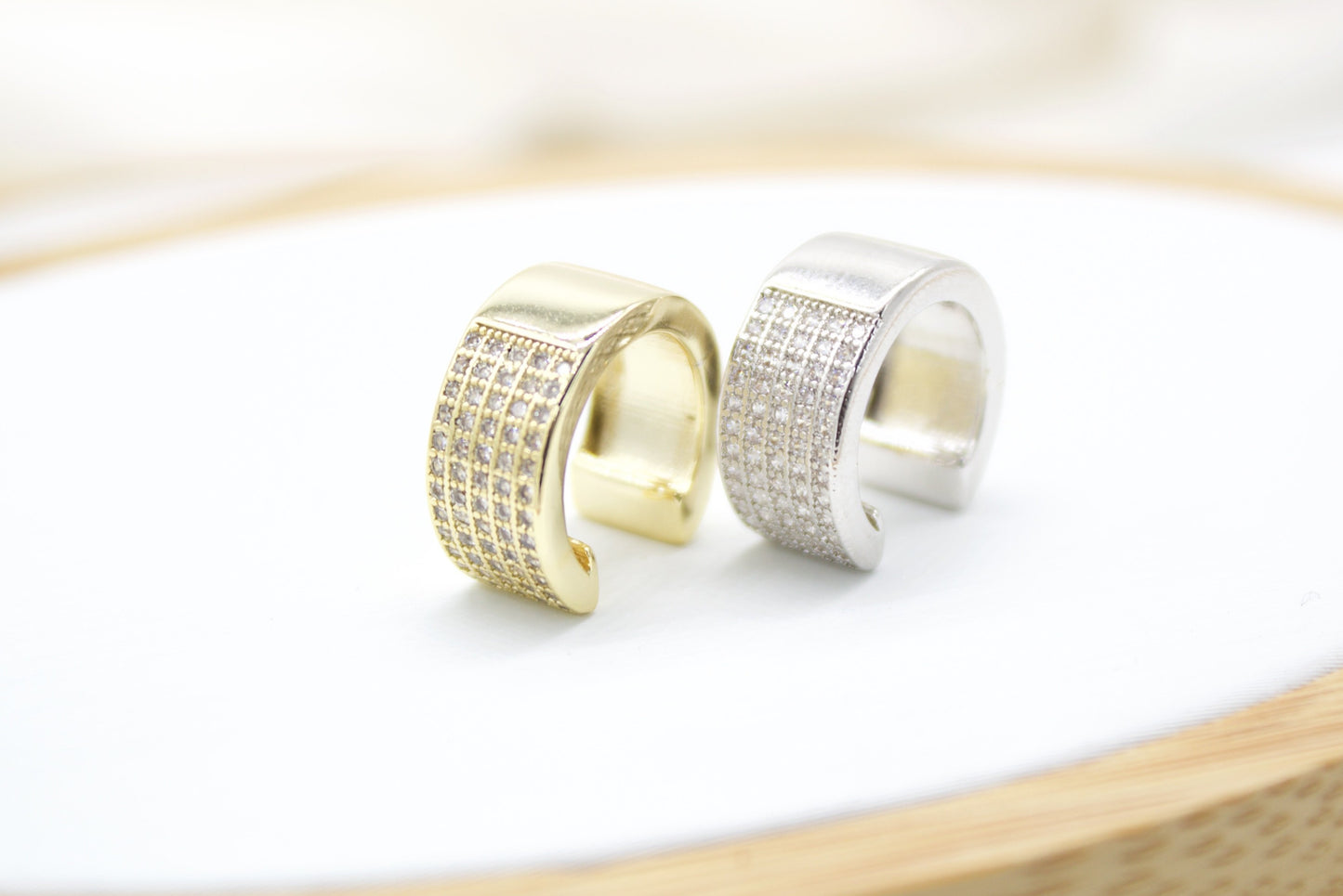 A gold and silver pave ear cuff rest side by side on a clean white surface.