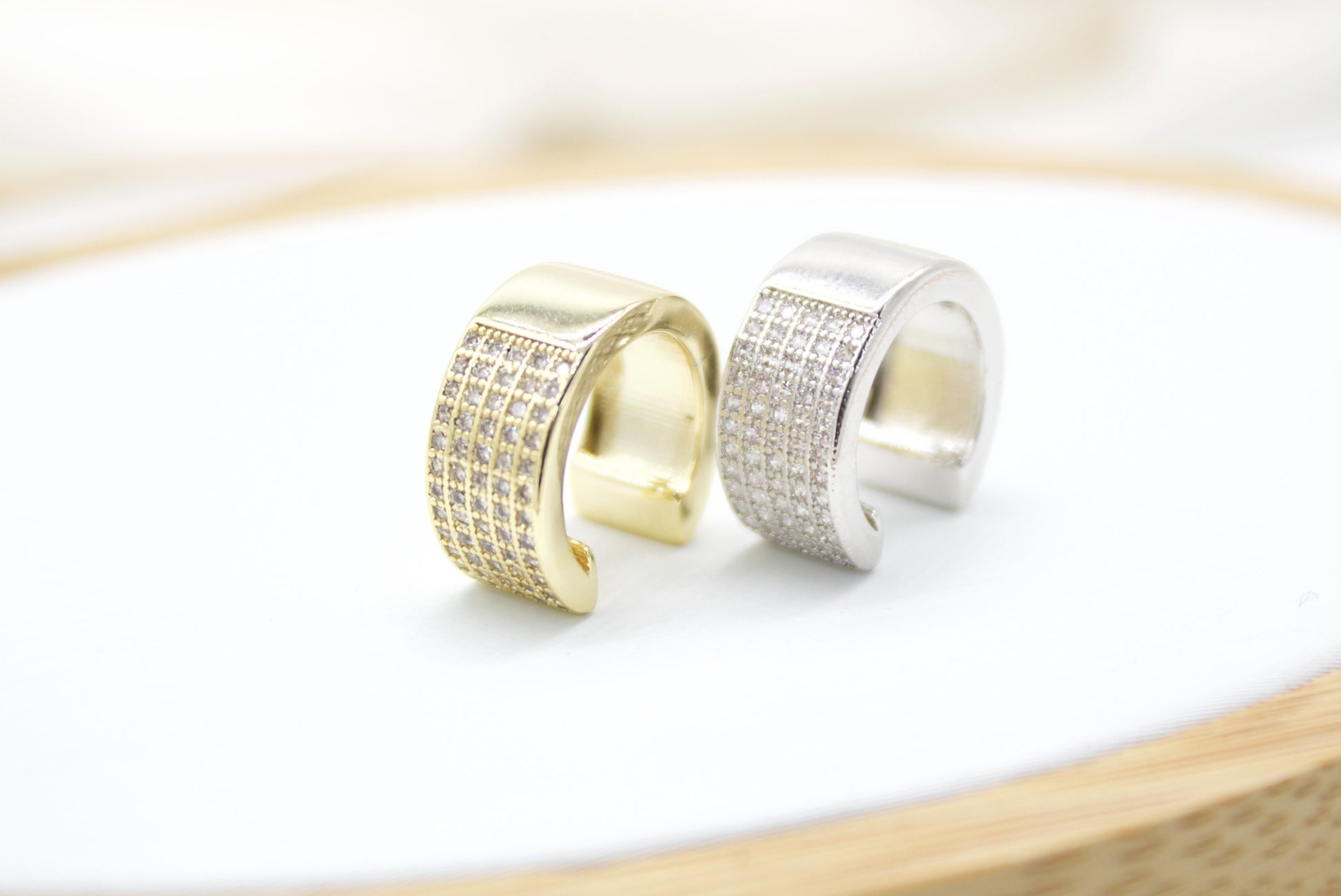 A gold and silver pave ear cuff rest side by side on a clean white surface.