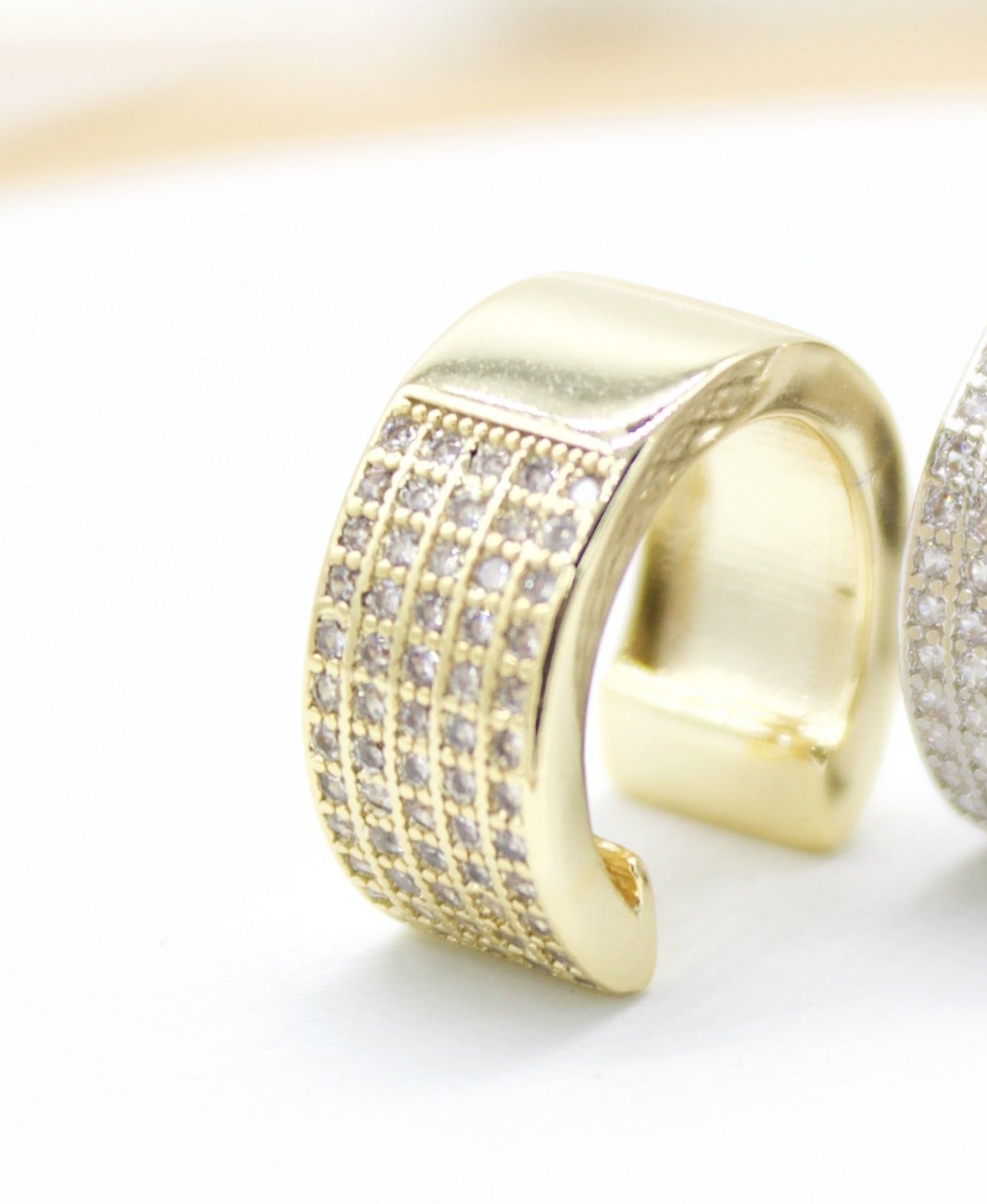 A thick gold ear cuff sparkles with rows of tiny, inlaid crystals on a white surface.