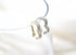 Two shimmering heart-shaped ear cuffs, one in gold and one in silver pavé-set with crystals, rest delicately on a transparent display loop against a soft white background.