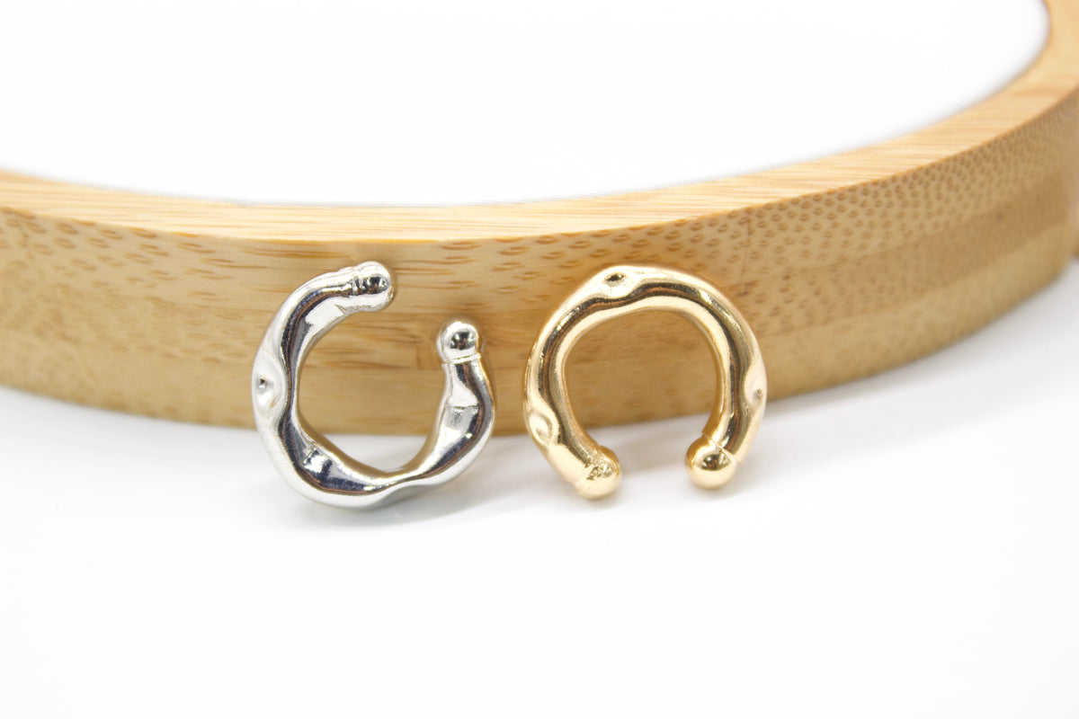 A silver and a gold organic-shaped cuff earring rest against a wooden display ring.