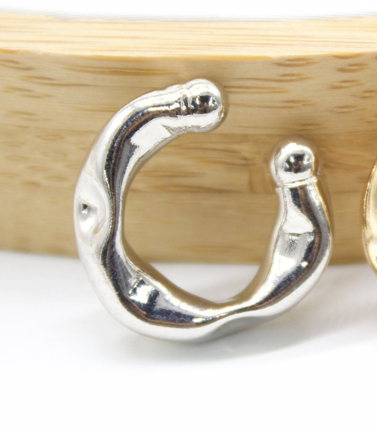A glossy silver ear cuff rests in front of a wooden background, showcasing its chunky, organic shape.