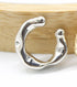 A glossy silver ear cuff rests in front of a wooden background, showcasing its chunky, organic shape.