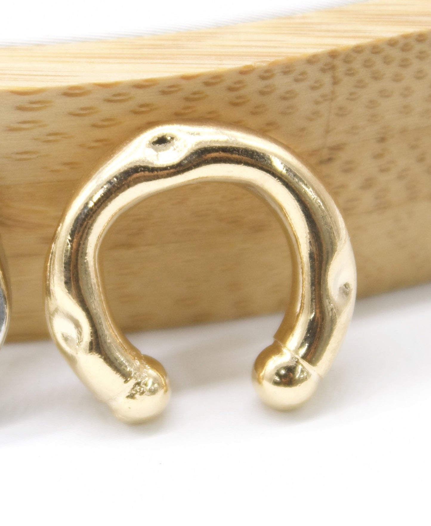 A glossy gold ear cuff rests against a textured wooden background.