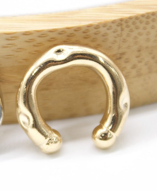 A glossy gold ear cuff rests against a textured wooden background.