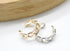Two interlocking chain-link ear cuffs, one gold and one silver, rest on a clean white surface beneath a wooden display.