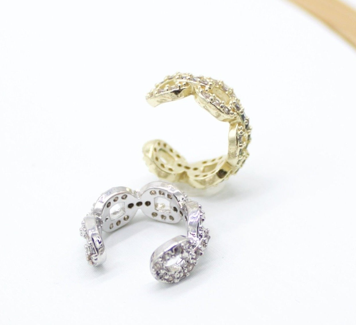A silver and a gold pave ear cuff rest side by side on a clean white surface.