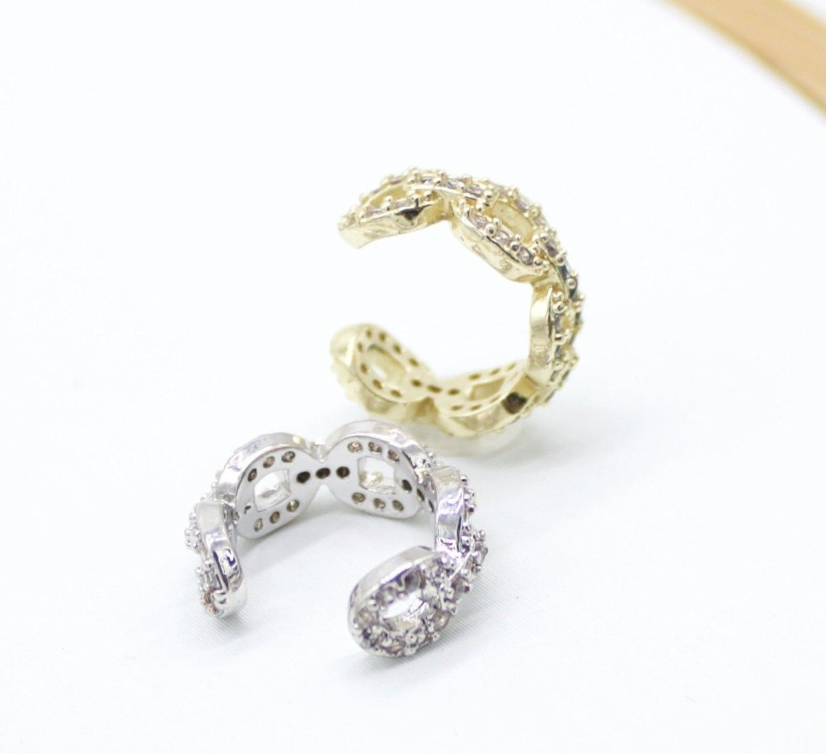 A silver and a gold pave ear cuff rest side by side on a clean white surface.