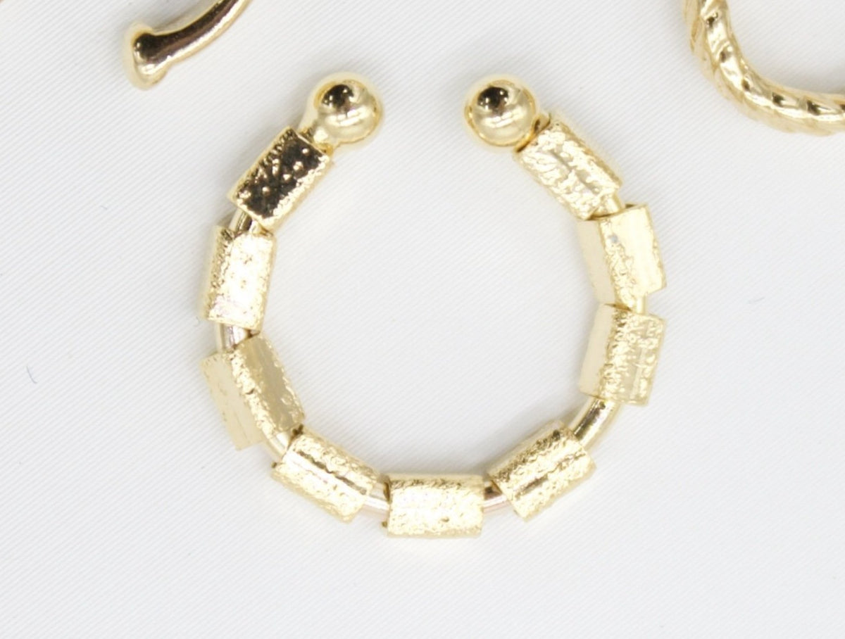 A gold textured geometric ear cuff rests on a white surface.