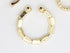 A gold textured geometric ear cuff rests on a white surface.