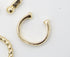A minimalist gold ear cuff rests on a white background alongside other gold jewelry pieces.