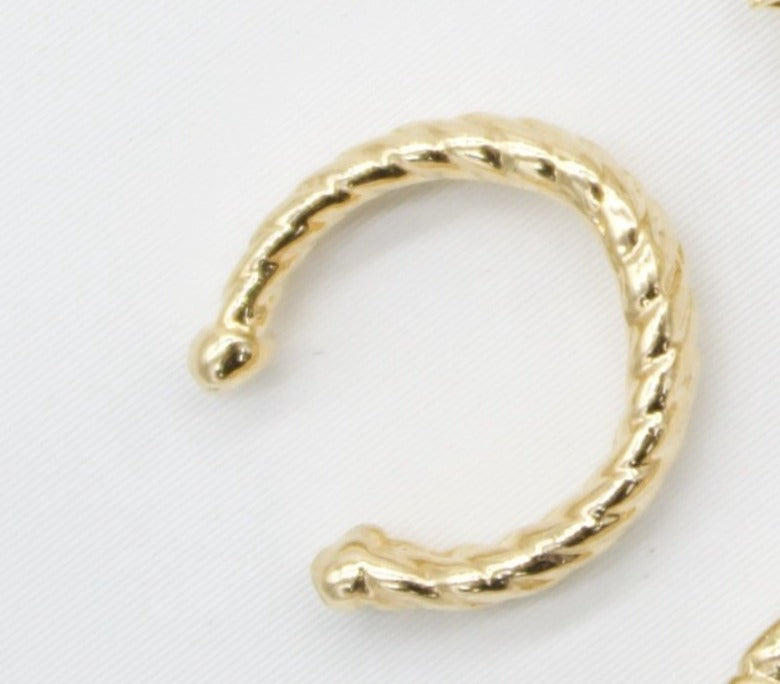 A polished gold ear cuff features a textured, twisted rope design against a clean white background.