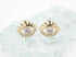 A pair of gold evil eye stud earrings featuring sparkling cubic zirconia crystals rests on a textured glass surface.