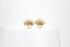 A pair of shiny gold seashell stud earrings rests on a glass surface against a clean white background.