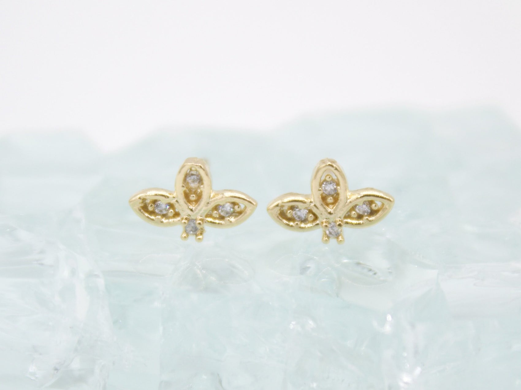 A pair of gold butterfly stud earrings rests on a textured light surface.