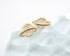 A pair of gold planet-shaped stud earrings featuring sparkling cubic zirconia details rests on a transparent crystal surface.