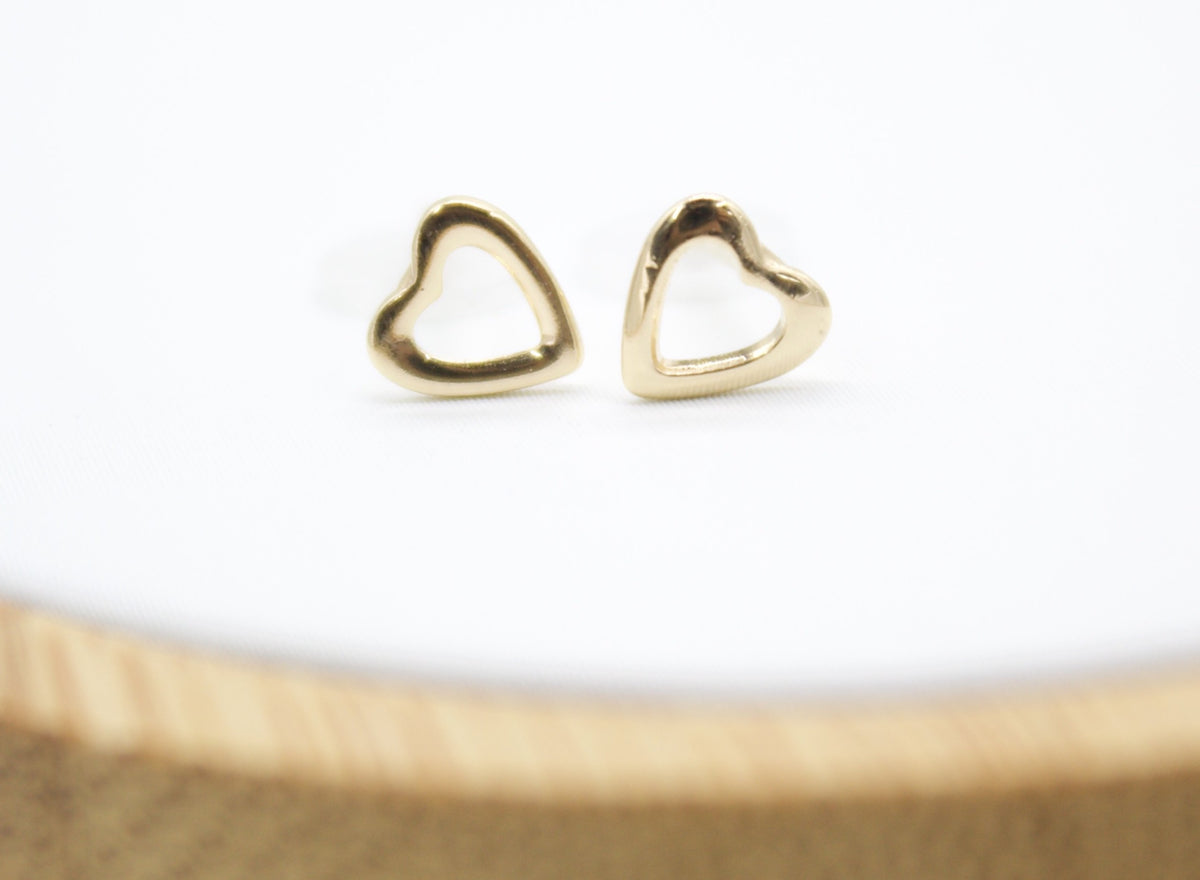 A pair of polished gold heart-shaped stud earrings rests neatly on a clean white surface.