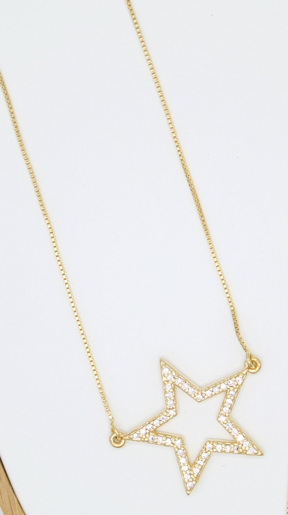 A delicate gold star pendant necklace sparkles with embedded cubic zirconia stones against a neutral background.
