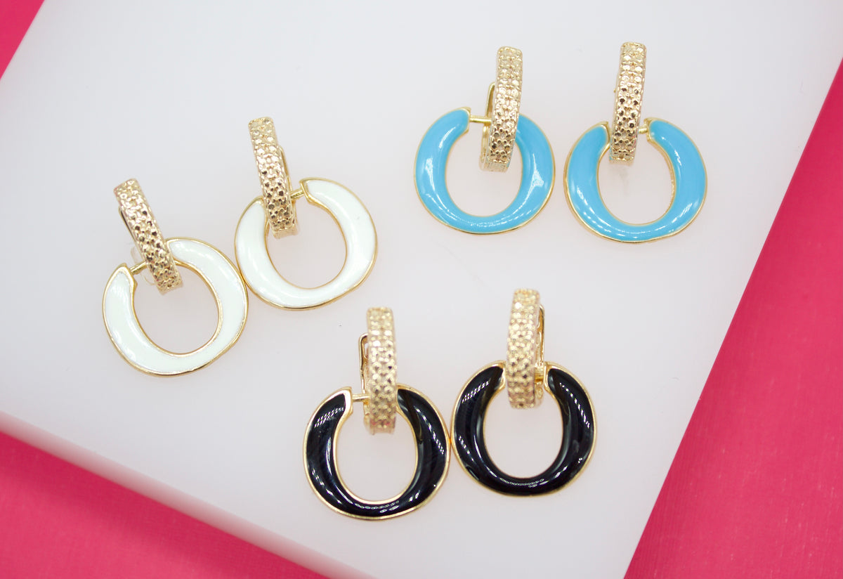 Three pairs of gold hoop earrings with white, blue, and black enamel accents rest on a white surface.