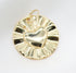 A shiny gold pendant features a raised puffy heart design centered on a round, sunburst-patterned disc resting against a white textured background.