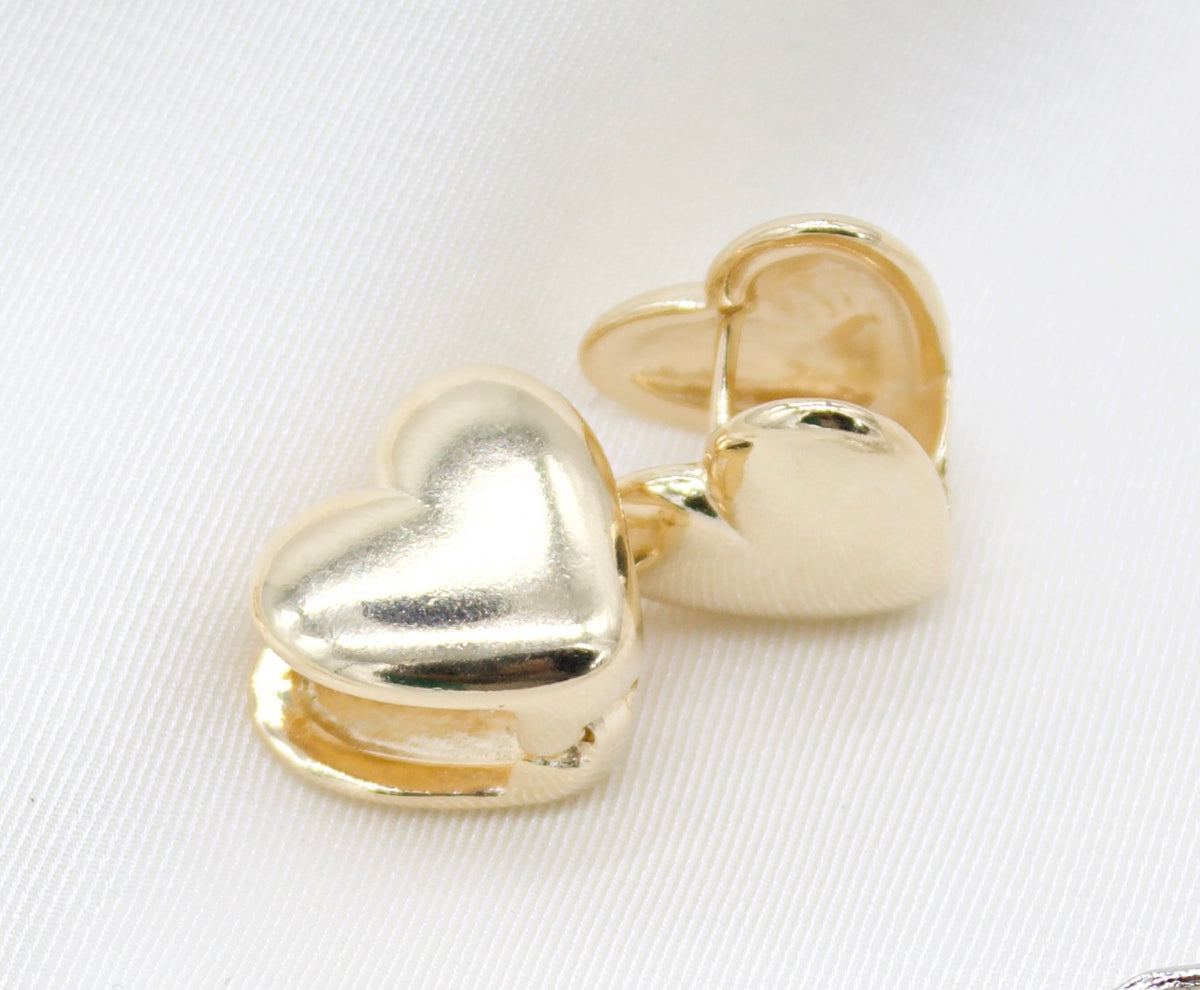 A pair of glossy gold heart-shaped hoop earrings rests on a white satin background.