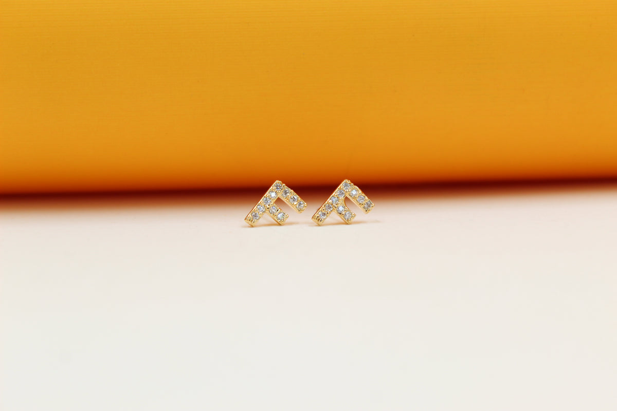Two gold initial F stud earrings sparkle with embedded cubic zirconia stones against a dual-toned backdrop.