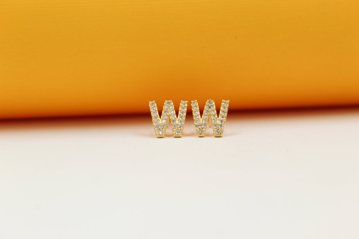 A pair of gold initial W earrings embellished with sparkling cubic zirconia stones rests against a vibrant orange and white backdrop.