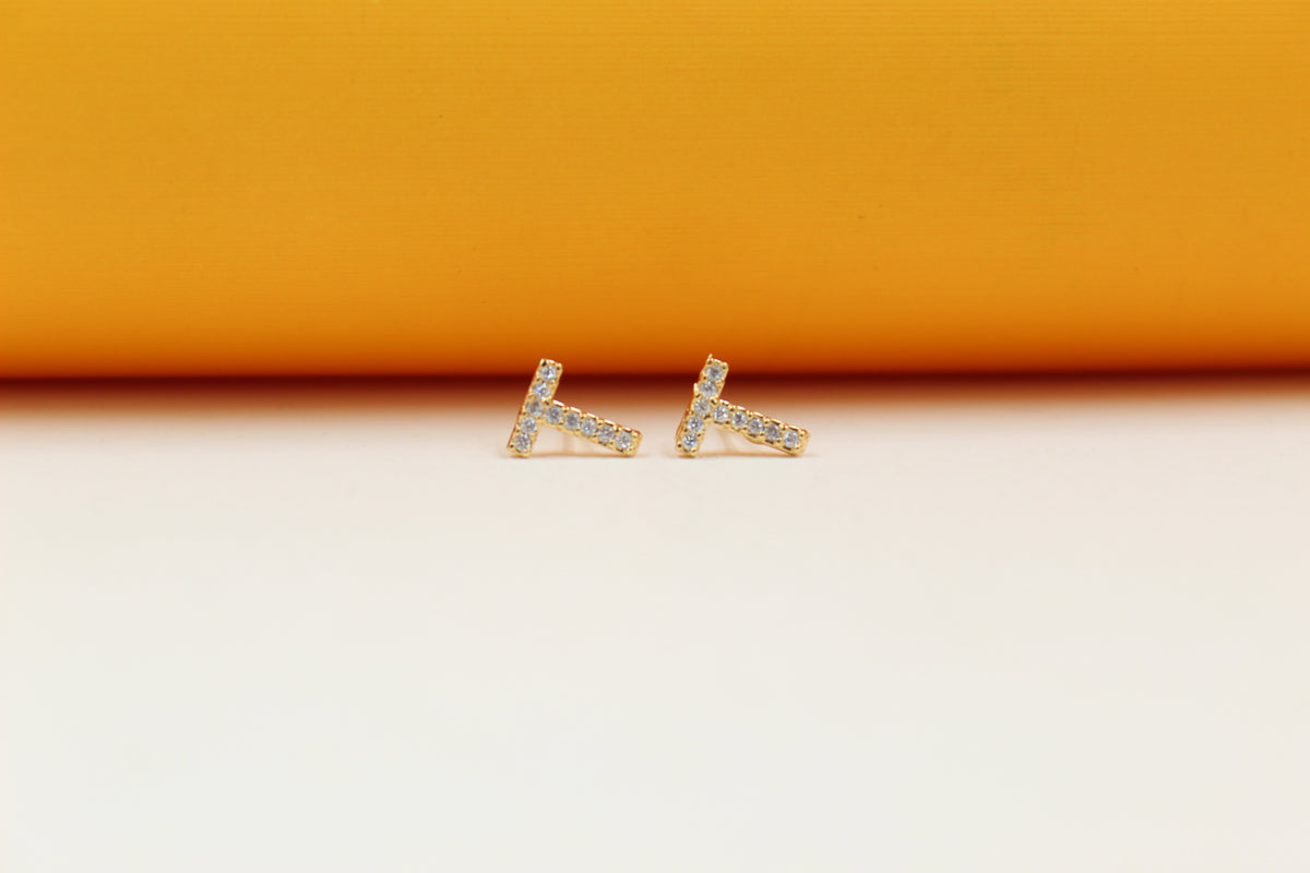 A pair of gold initial T stud earrings sparkle with embedded cubic zirconia stones against a neutral backdrop.