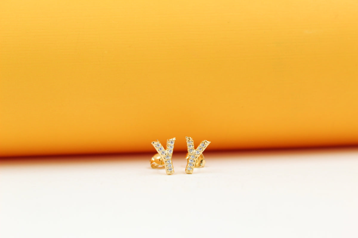 A pair of gold initial Y stud earrings sparkle against a vibrant orange and white background.