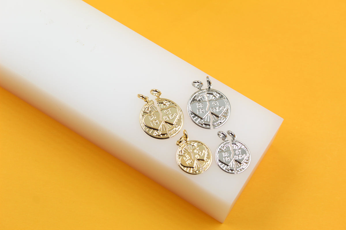 Four gold and silver "Best Friends" split heart pendant charms rest on a white block against a bright yellow background.