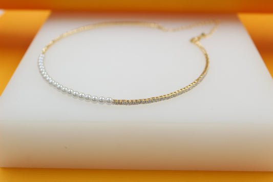 A delicate gold necklace featuring a half-pearl and half-diamond tennis chain rests elegantly on a white display surface.