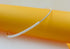 A delicate necklace featuring a row of white pearls transitioning into a sparkly diamond-encrusted band rests against a bright yellow cylinder.