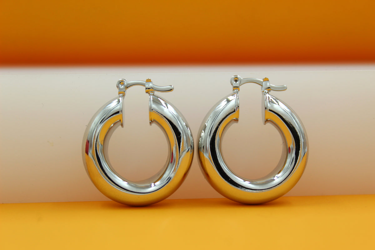 A pair of thick silver hoop earrings rests on a multi-colored background.