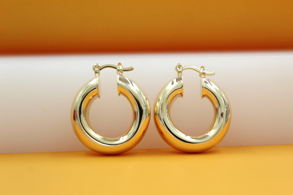 Two thick, polished gold hoop earrings rest side by side on a minimalist white and orange background.