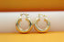 Two thick, polished gold hoop earrings rest side by side on a minimalist white and orange background.