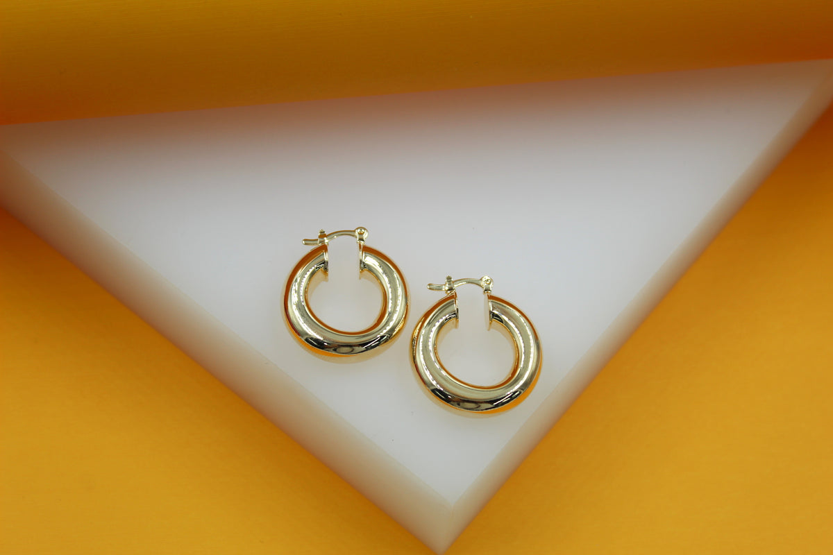 A pair of polished gold hoop earrings rests elegantly on a geometric white and yellow display stand.