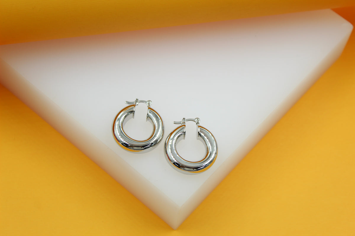 Two shiny silver hoop earrings rest neatly on a white and yellow geometric display block.