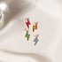 Four colorful enamel lightning bolt charms in red, orange, green, and blue rest on a white silk background.