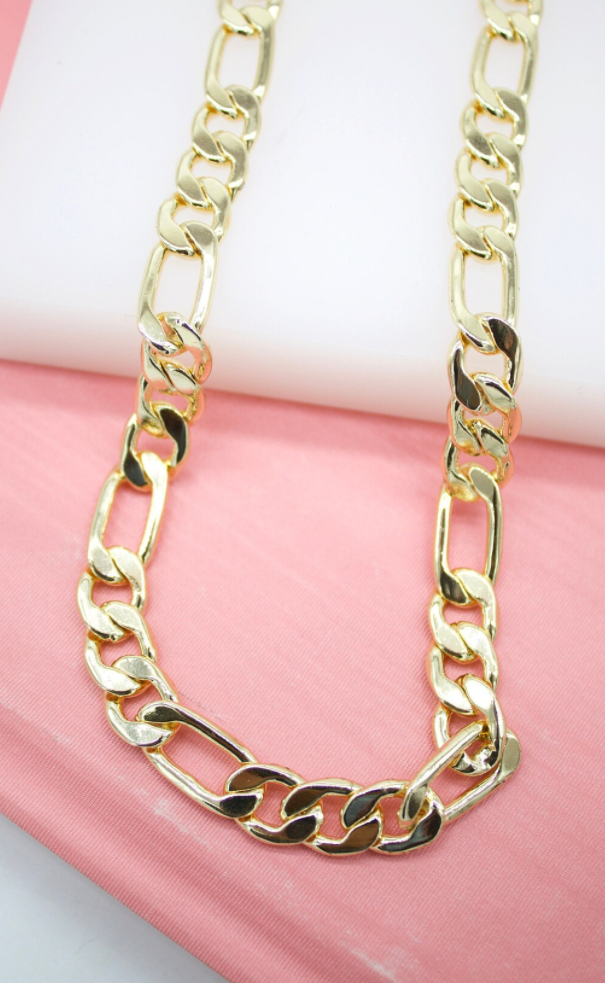 A shiny gold Figaro chain necklace rests on a pink and white background.