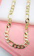 A shiny gold Figaro chain necklace rests on a pink and white background.