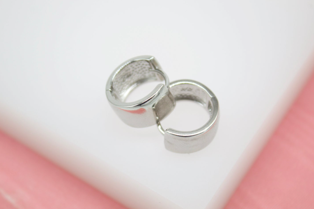 A pair of polished silver hoop earrings rests against a white and pink background.