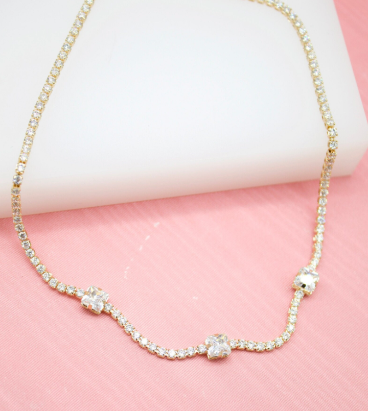 A delicate gold tennis necklace features a continuous line of sparkling diamonds set against a soft pink background.