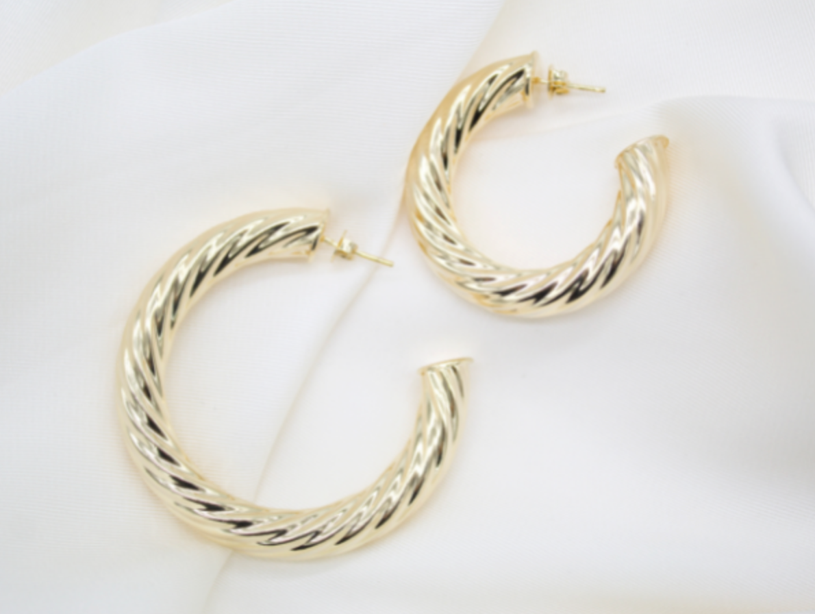 Two polished gold twisted hoop earrings rest elegantly on a soft white silk fabric.