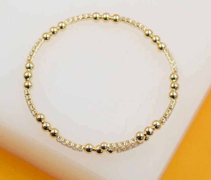 A delicate gold bead and crystal stretch bracelet rests gracefully on a neutral white display surface.