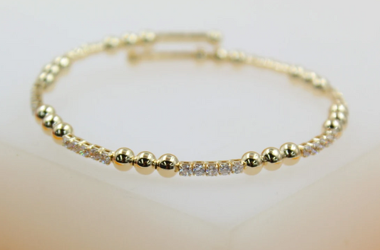 A delicate gold beaded bracelet with alternating sections of polished gold spheres and sparkling cubic zirconia stones rests on a light surface.