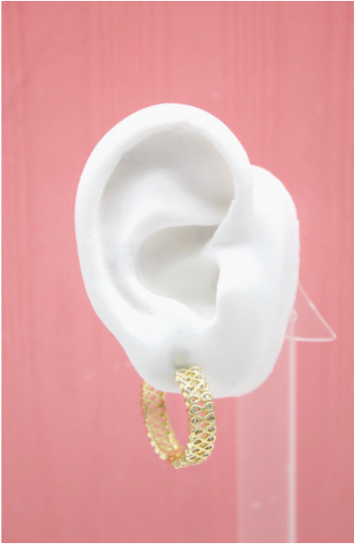 A white mannequin ear displays a textured gold hoop earring encrusted with small clear stones against a pink background.