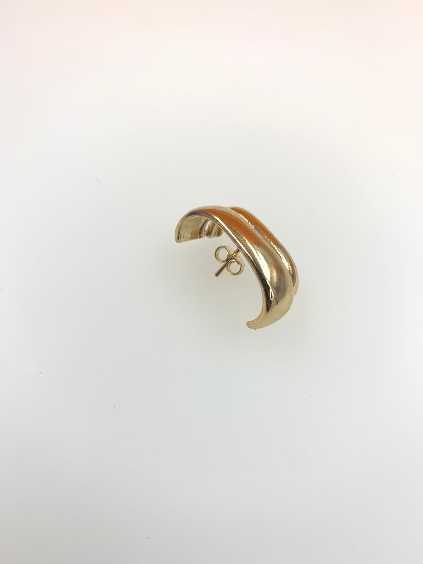 A sleek gold dome huggie earring rests against a neutral white background.