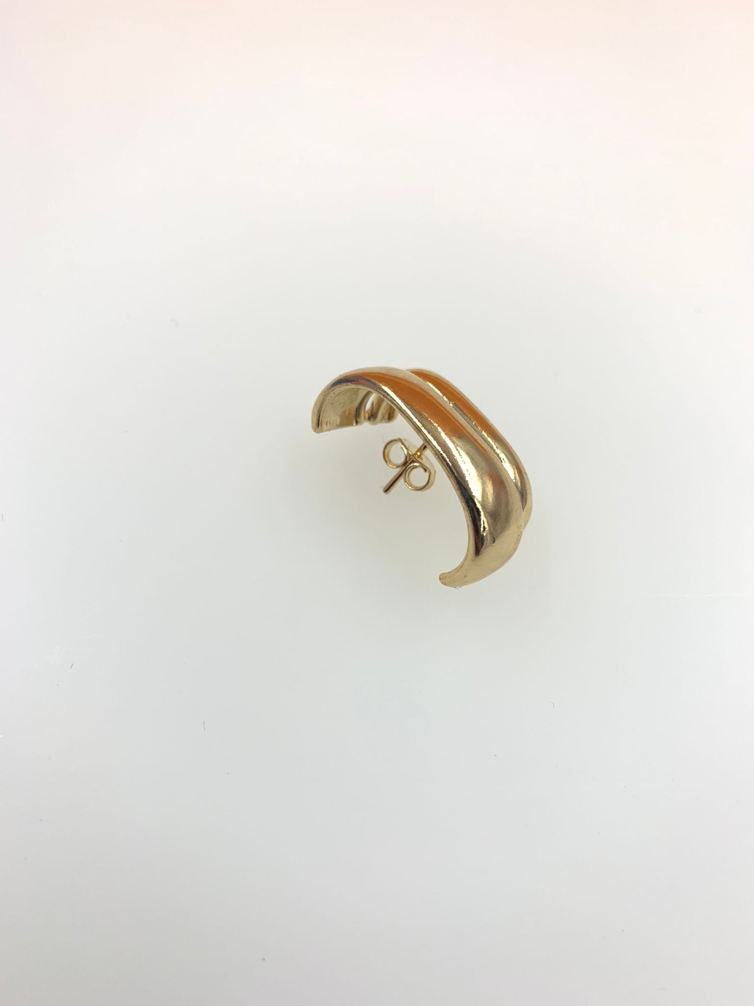 A sleek gold dome huggie earring rests against a neutral white background.